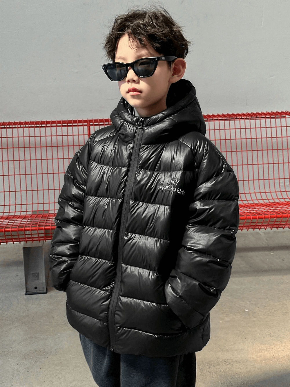 Boy wearing Hooded Puffer Jacket with Zipper and Insulation - SF3640, black color, hands in pockets, standing by red bench