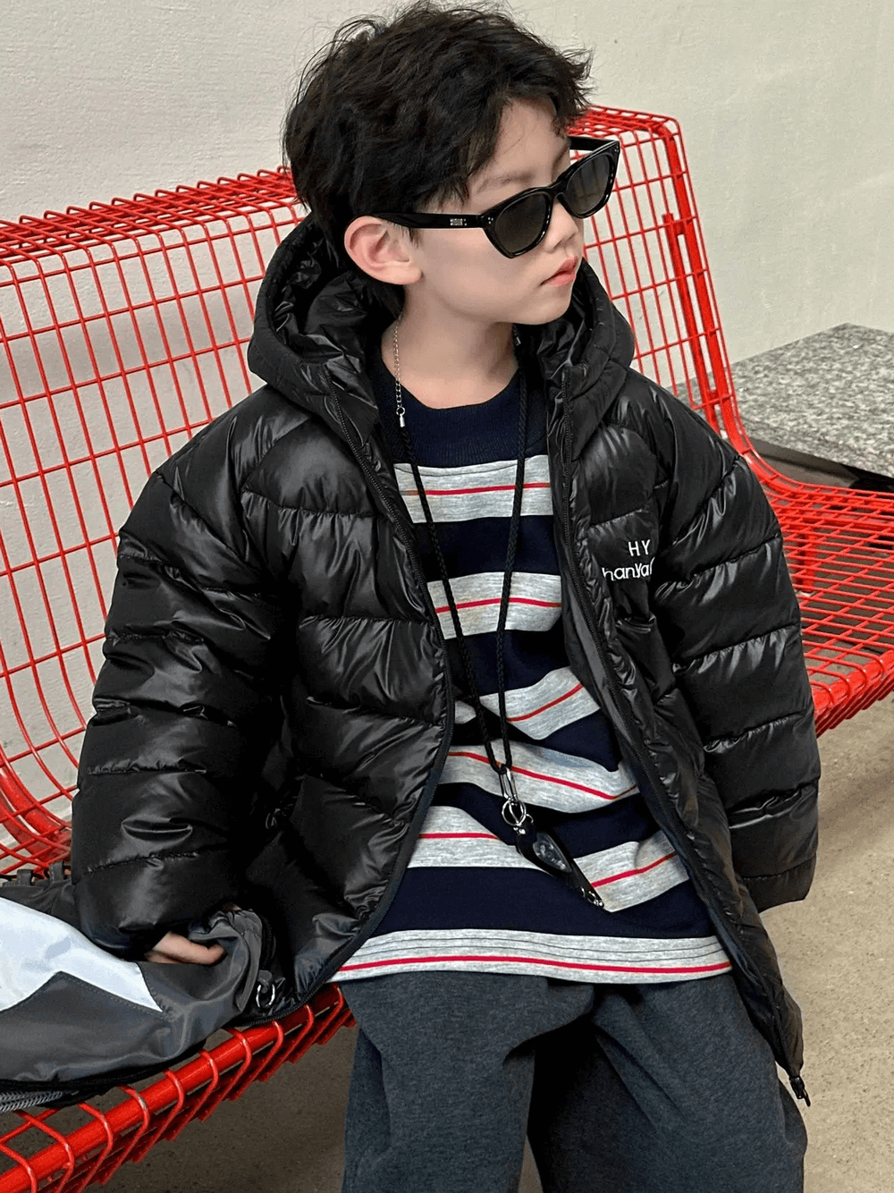 Boy wearing Hooded Puffer Jacket with Zipper and Insulation - SF3640, sitting on a red chair, stylish and warm winter coat.