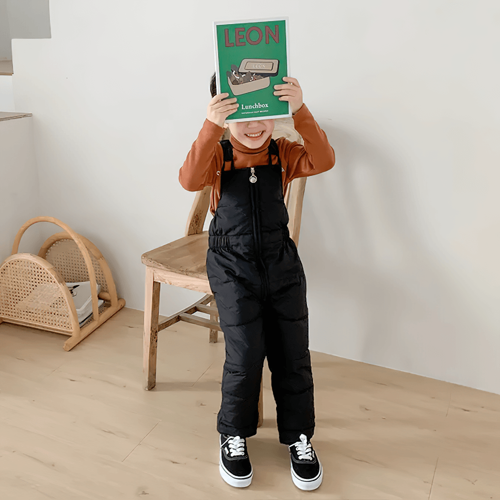 Child wearing Insulated Snow Bib Pants for Boys and Girls - SF3731, holding a book, in cozy indoor setting.
