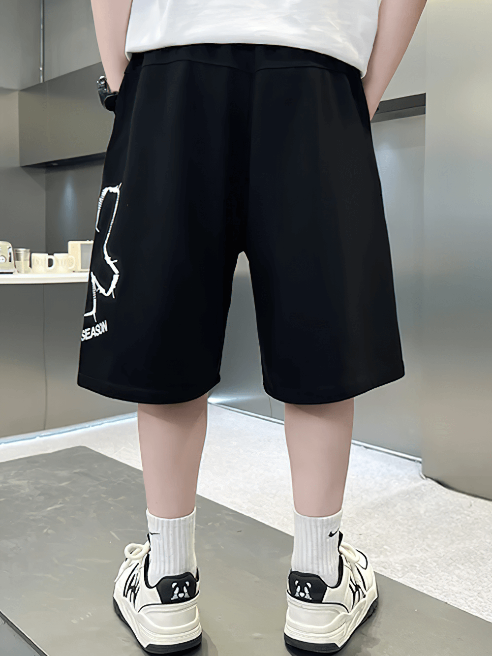 Back view of black Kids Baggy Cotton Shorts with Graphic Print - SF3891, showcasing casual fit with white sneakers.
