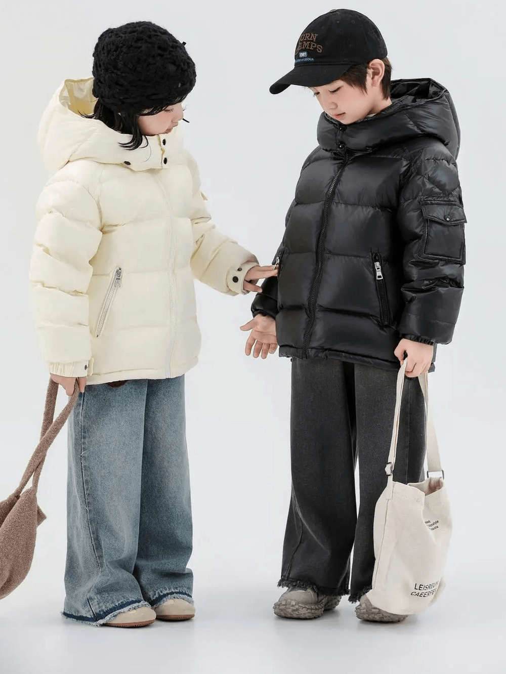 Two children wearing Kids Duck Down Jacket with Hood and Zipper - SF3515, one in white and the other in black, standing with bags.