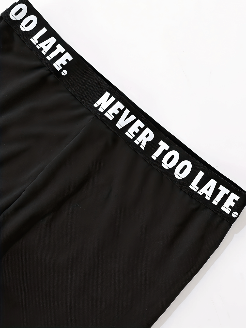 Close-up of the "Never Too Late" design on black sports leggings waistband, emphasizing motivational athletic wear message.