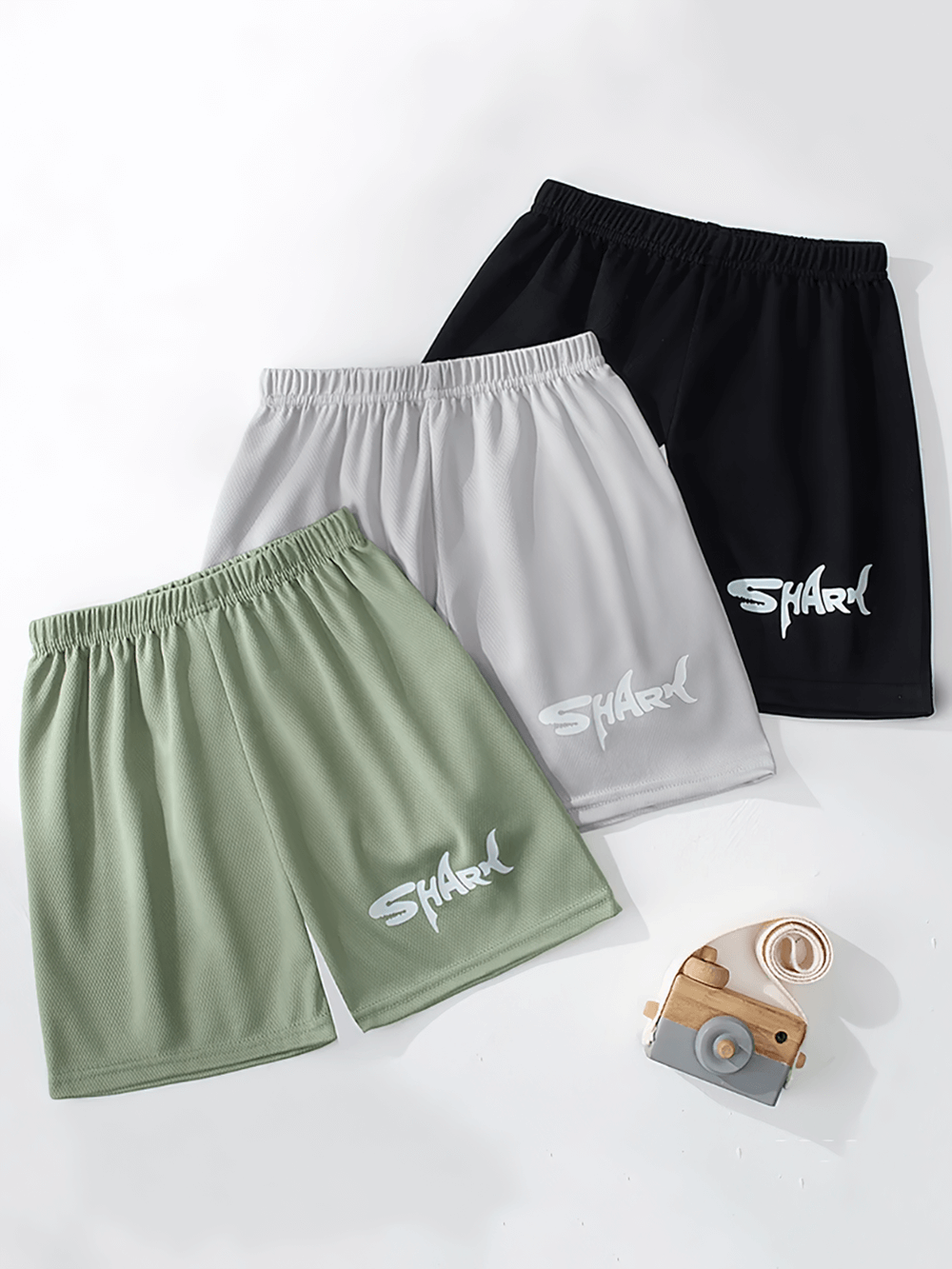 Three pairs of quick-drying sport shorts in green, grey, and black with shark print, perfect for kids' active wear.