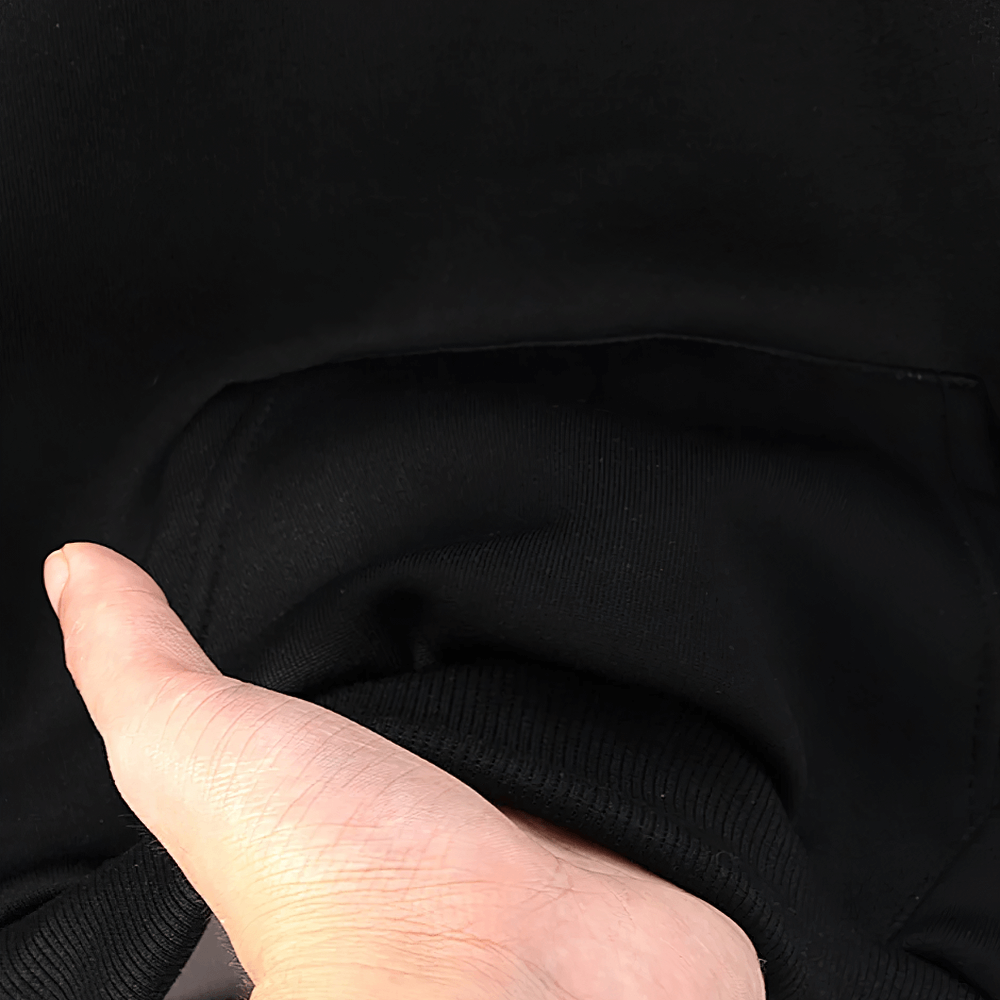 Close-up of a hand placing an object in the front pocket of a kid's black pullover hoodie, showcasing its handy storage feature.
