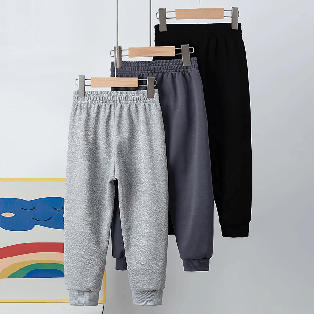 Three colors of Kids Sport Jogger Sweatpants with Elastic Waist - SF3888 hanging on wooden hangers.