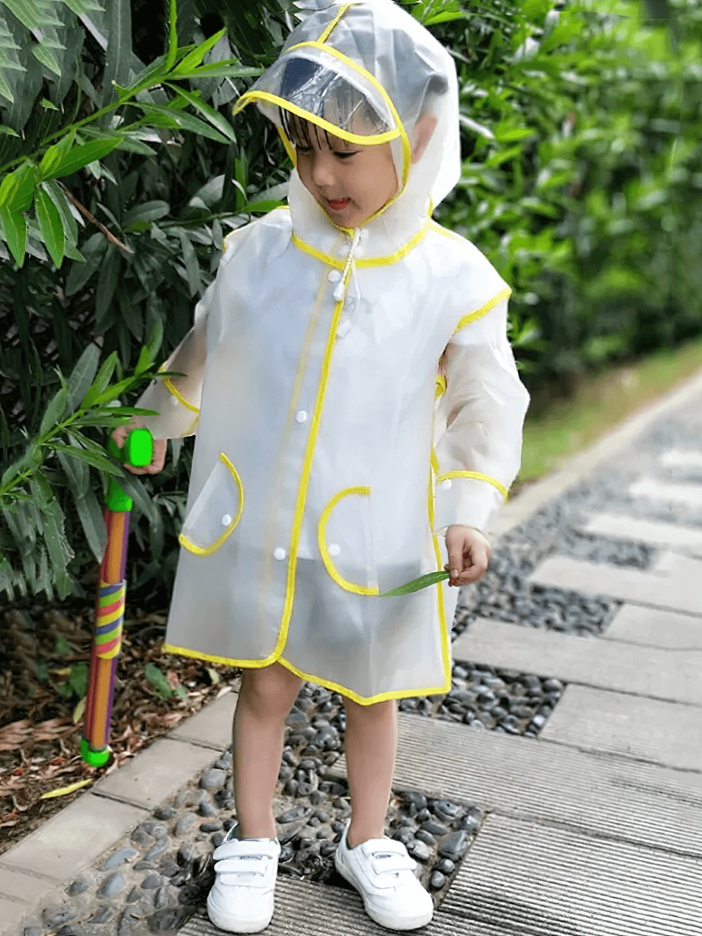 Child wearing Kids Transparent Long Hooded Raincoat - SF3671 with yellow trim and visor, holding an umbrella, enjoying a rainy day.