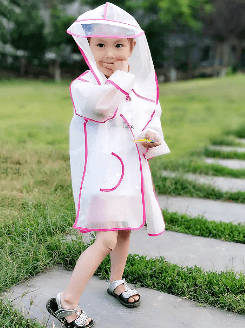 Child wearing Kids Transparent Long Hooded Raincoat - SF3671 with pink trim, enjoying a rainy day outdoors.