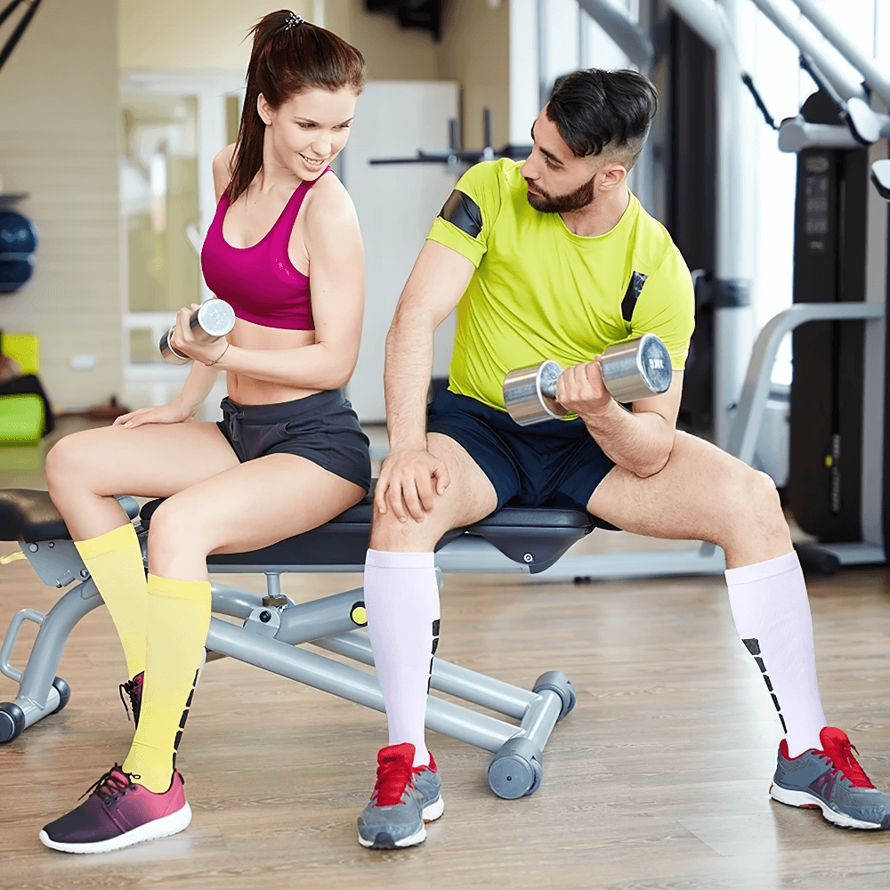 Two athletes wearing colorful knee-high compression socks while lifting weights in the gym, showcasing performance-enhancing sports gear.