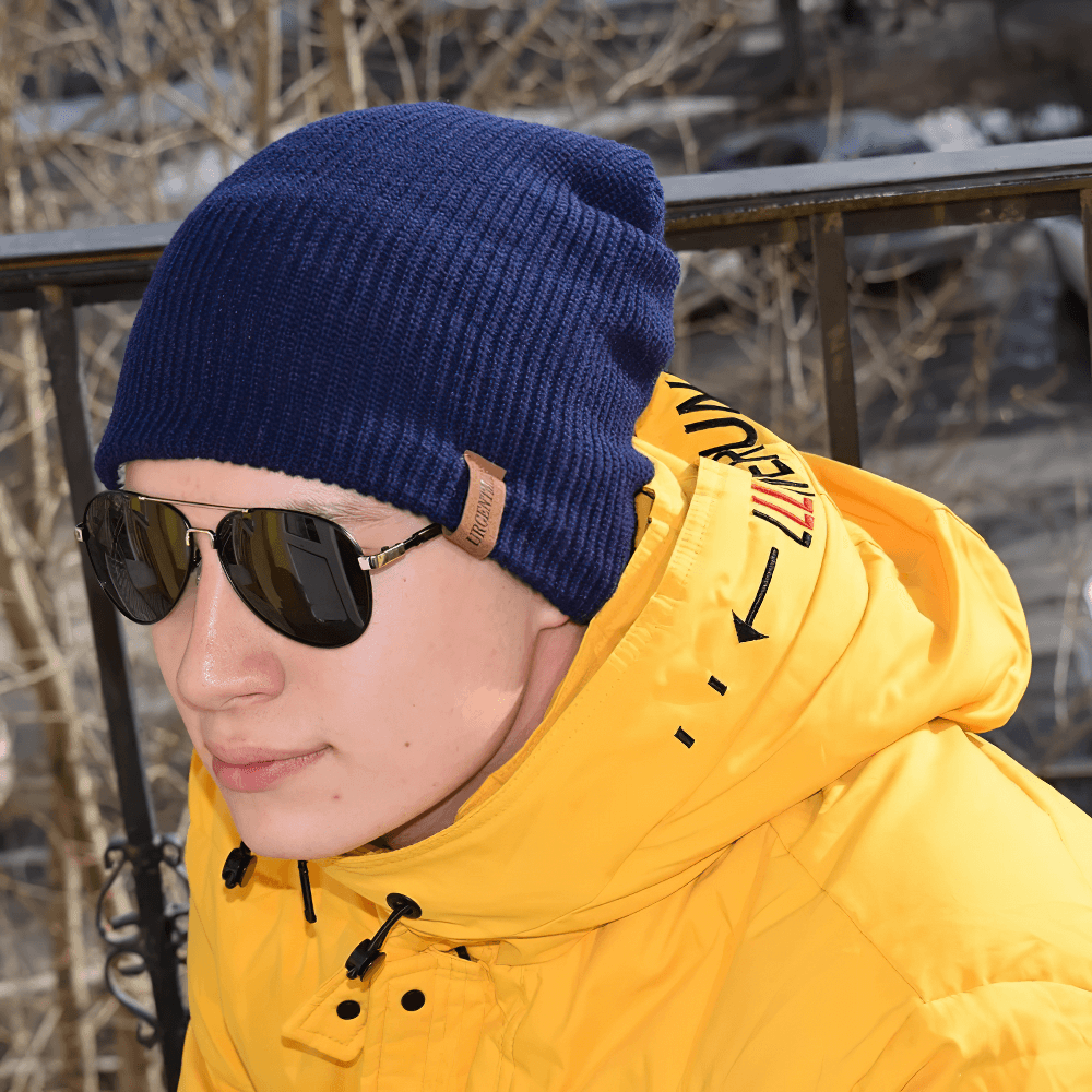 Person wearing knitted winter beanie hat, unisex, fur-lined, paired with sunglasses and a yellow jacket outdoors.