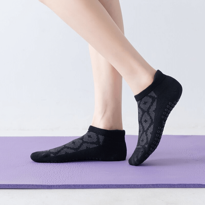 Black breathable anti-slip cotton Pilates socks on woman's feet on purple mat.
