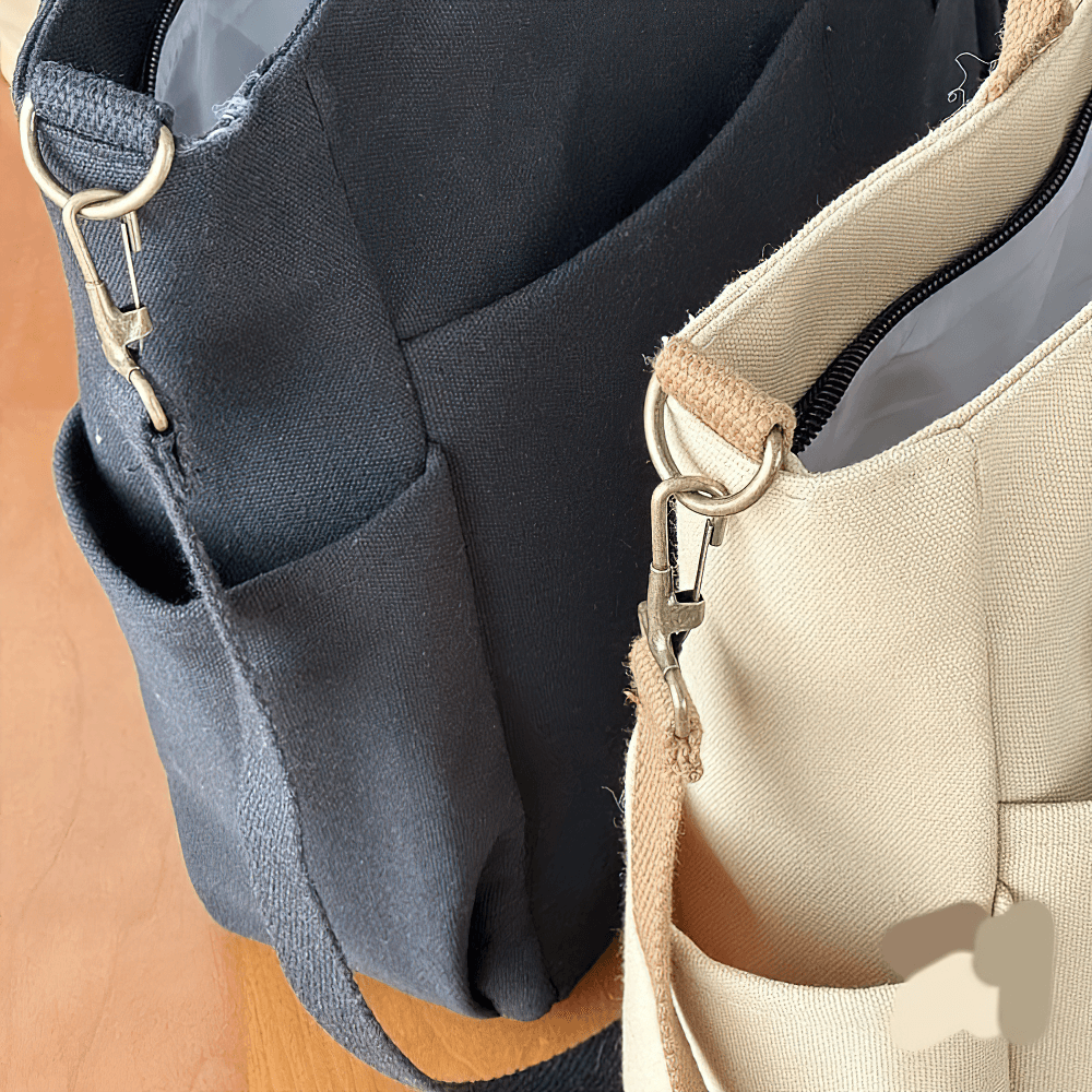 Close-up of two large canvas tote bags with multi-pocket design in black and beige colors, featuring durable adjustable straps.