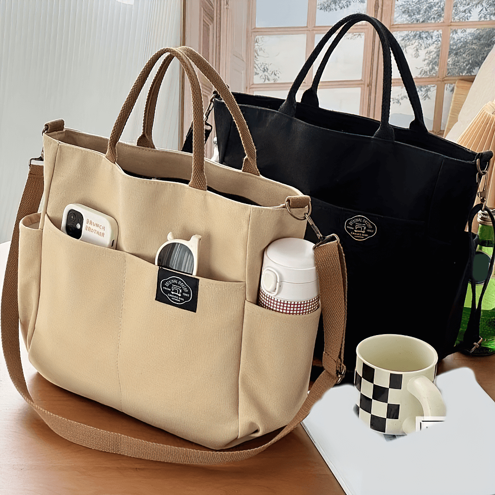 Large canvas tote bag with multi-pocket design in beige and black on a table, showcasing versatile shoulder and crossbody strap. SF2663 model.