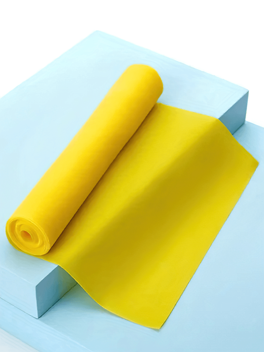 Yellow latex resistance band for yoga and Pilates on a light blue surface, rolled and ready for home workout and physical therapy.