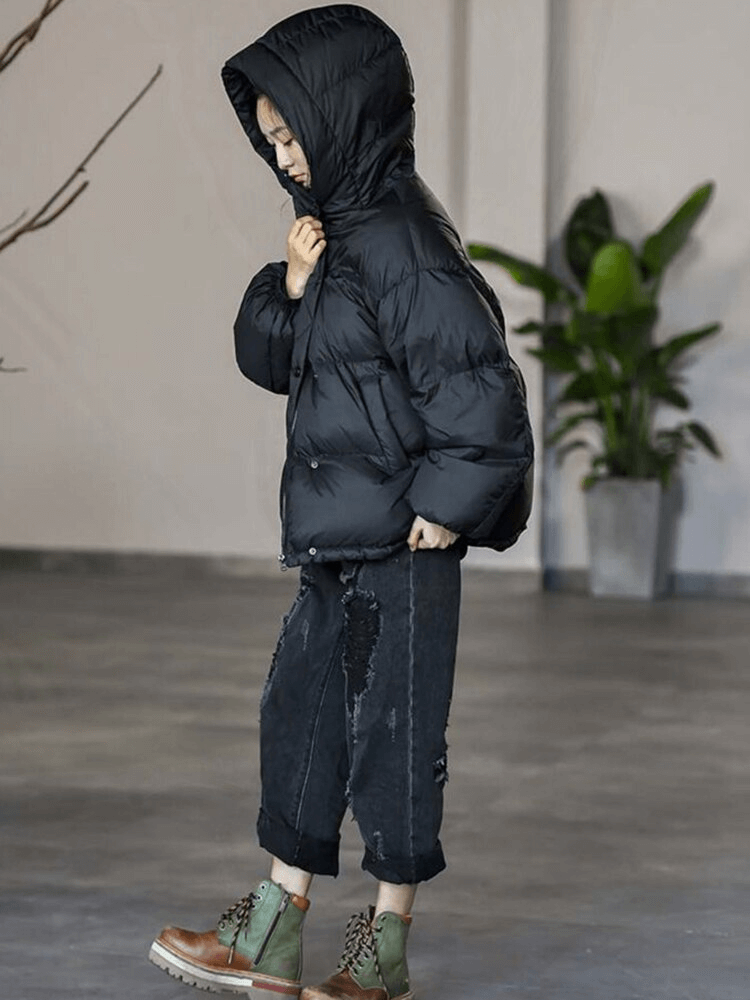 Child wearing a black hooded puffer jacket and boots, standing indoors, showcasing winter fashion style.