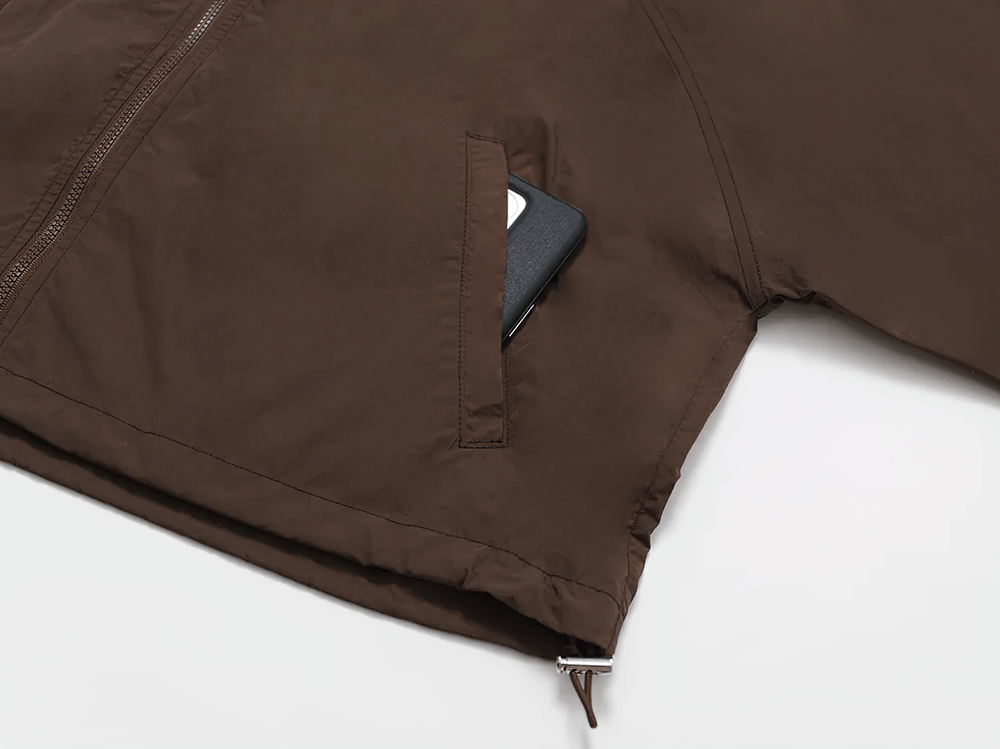 Close-up of brown lightweight windbreaker with pocket and adjustable drawcord hem, perfect for active outdoor wear.