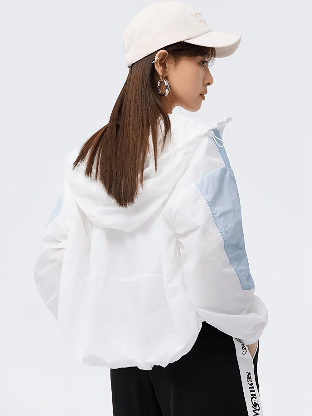 Stylish women's colorblock windbreaker with hood, shown from back view. Perfect for outdoor activities, model wearing casual cap.