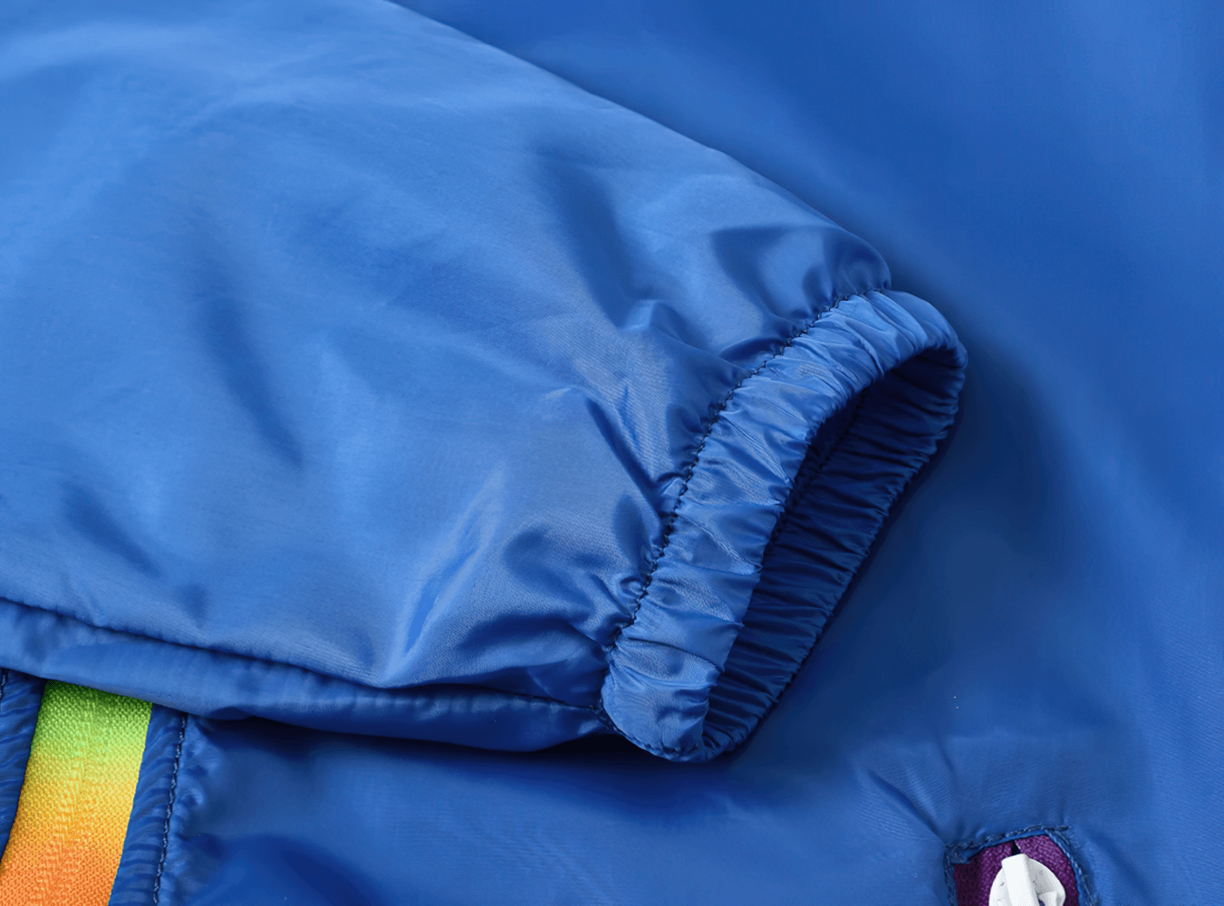 Close-up of blue Lightweight Hooded Windbreaker with Rainbow Zipper - SF3635, featuring elastic cuff and colorful zipper detail.