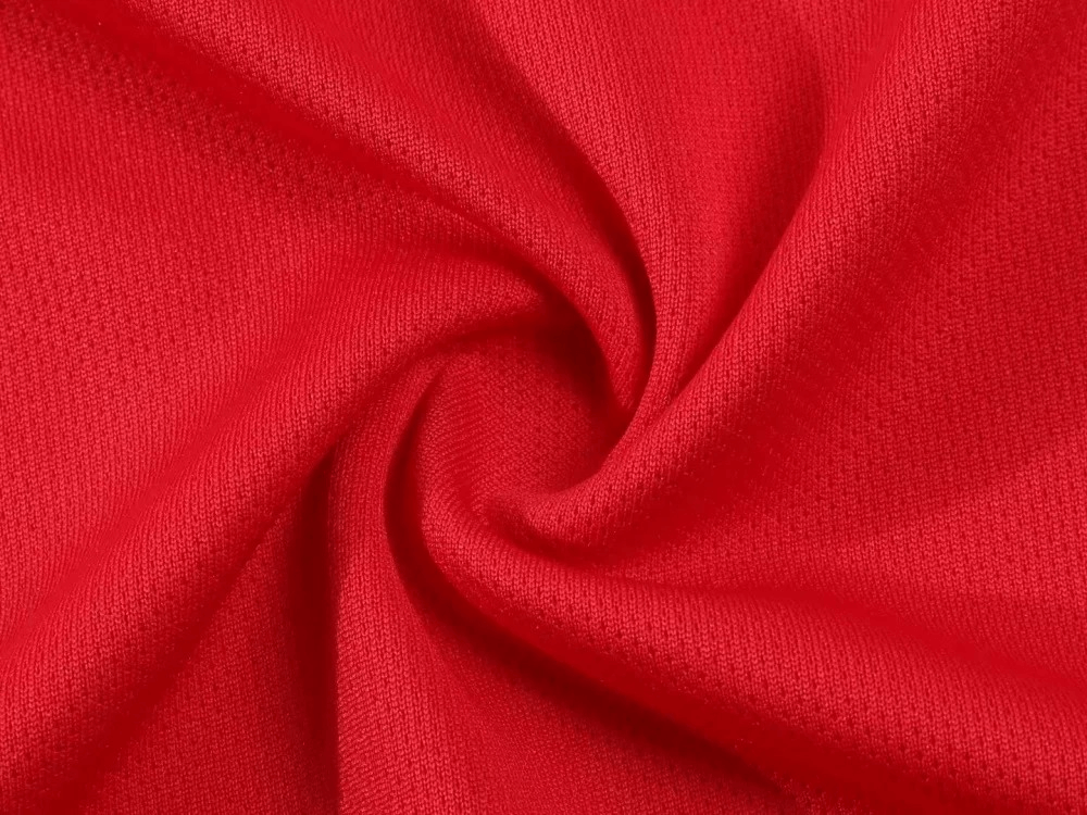 Close-up of red breathable polyester fabric, showcasing texture of athletic T-shirt and shorts set for men's fitness activities.