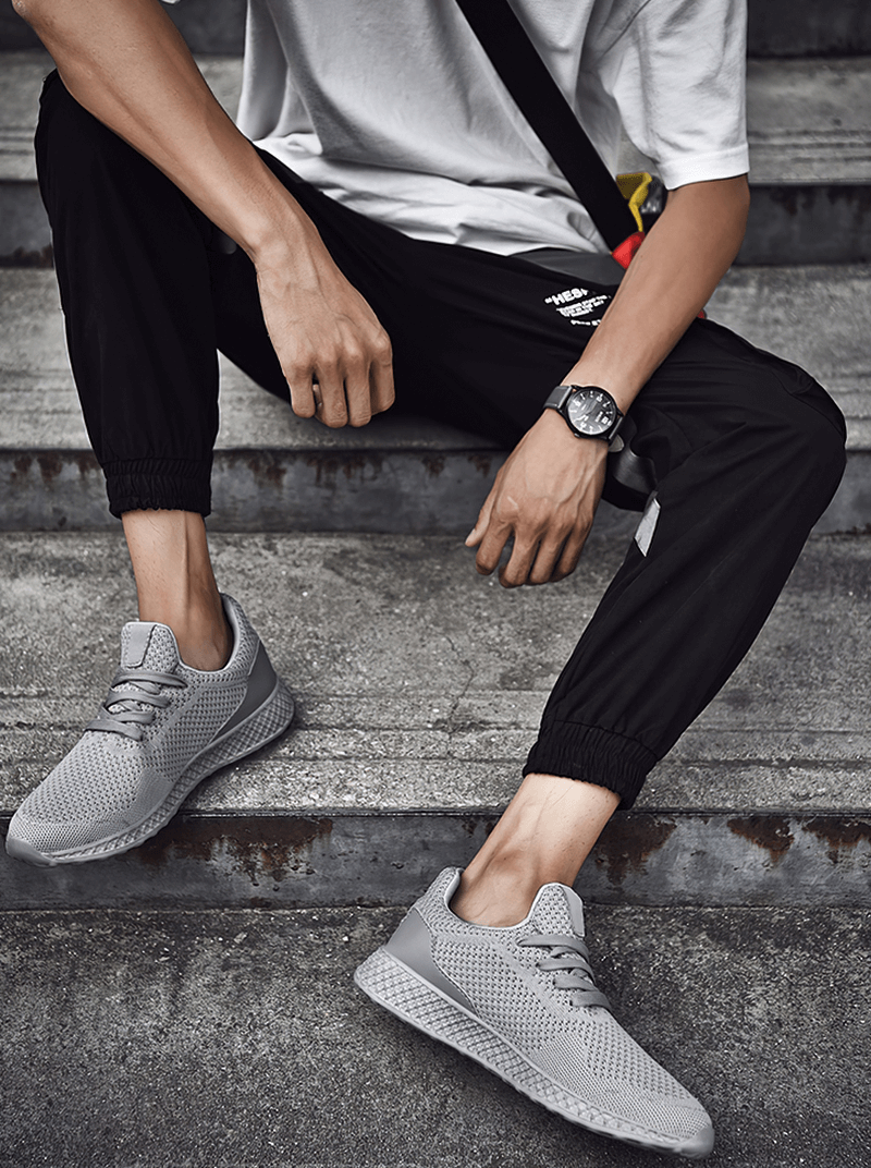 Man wearing lightweight mesh training shoes sitting on steps, showcasing breathable tennis shoes with EVA cushioning and rubber outsole.