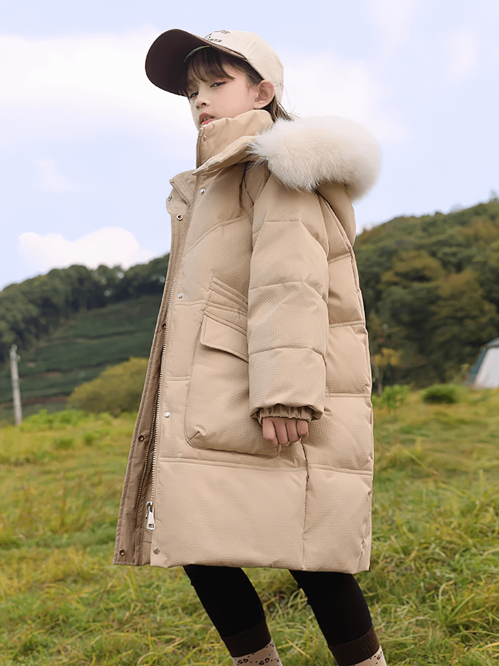 Girl wearing Long Down Coat with Hood and Faux Fur Trim - SF3525, beige puffer with large pockets in a scenic outdoor setting.