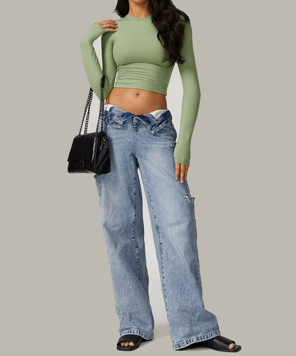 Woman wearing a green long sleeve sports crop top and denim jeans carrying a black handbag, perfect for yoga and fitness activities.