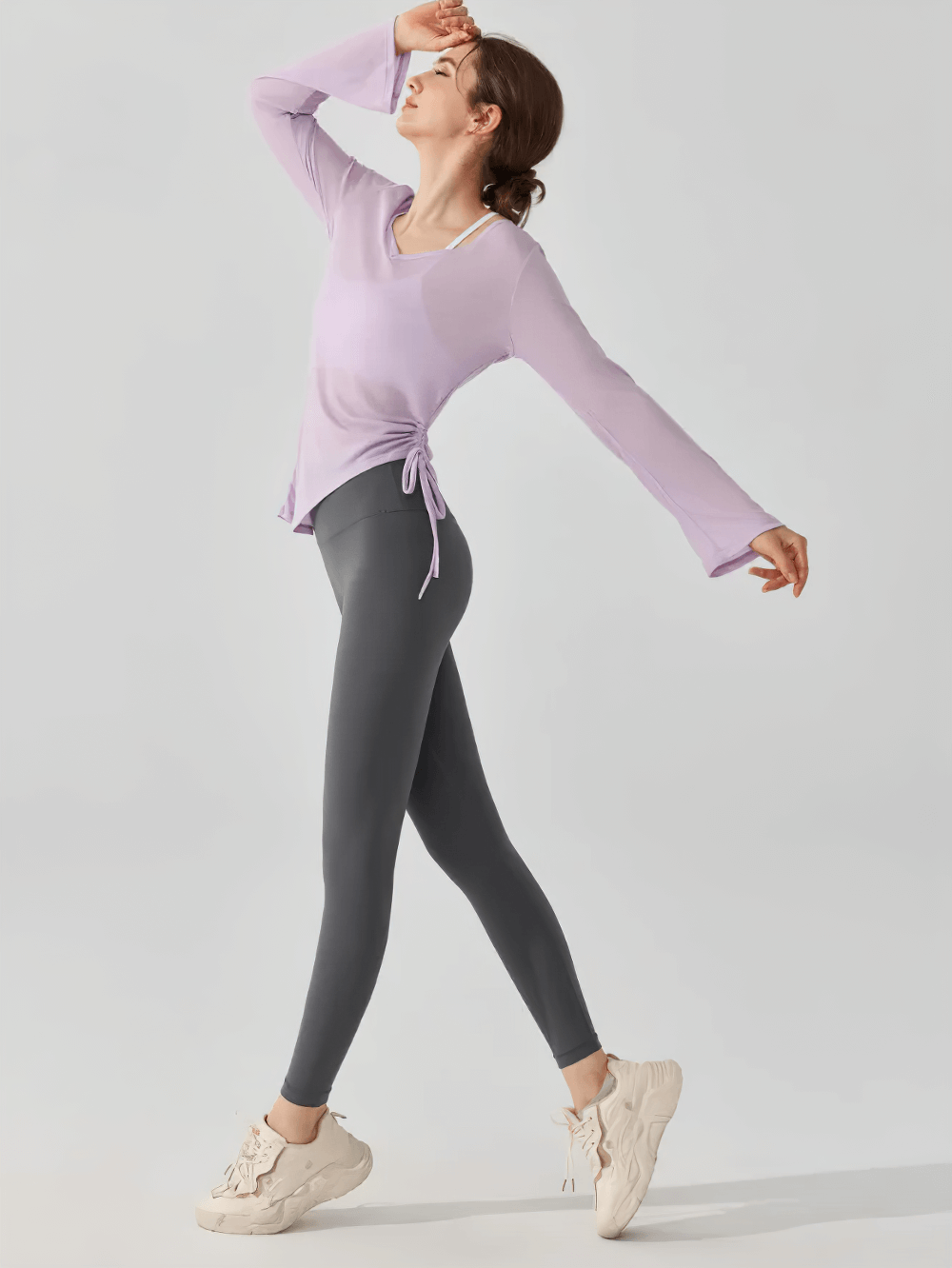 Woman wearing a long-sleeve yoga top with ruched side tie, paired with leggings. Ideal for yoga, fitness, and casual wear.