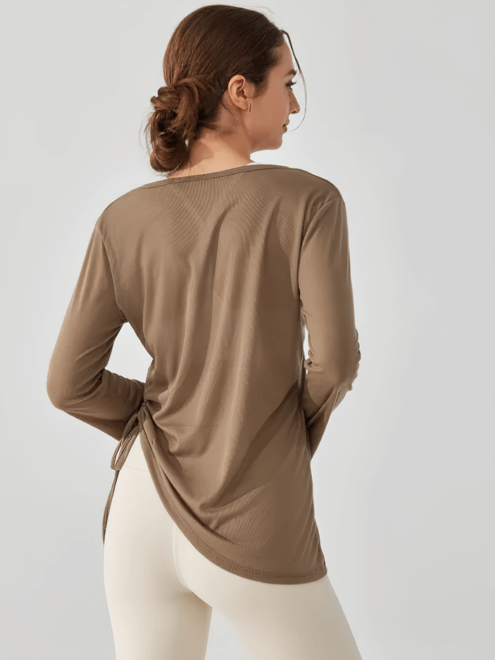 Woman wearing long-sleeve yoga top with ruched side-tie detail, ideal for yoga and training. V-neck activewear shirt in lightweight fabric.