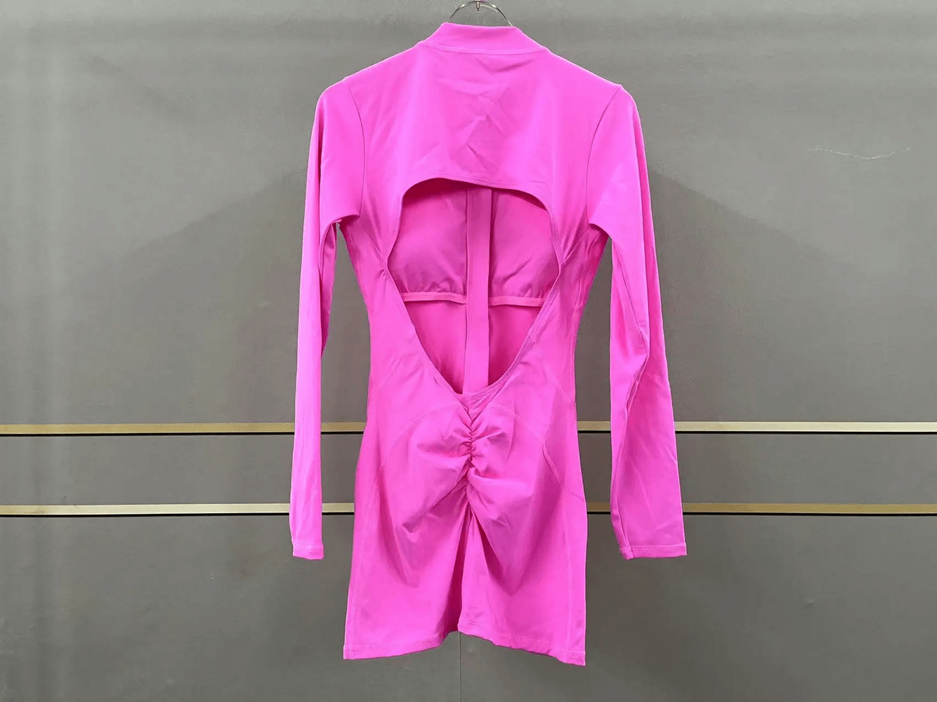 Pink long-sleeved romper with an open back design, showcasing stretchy fabric for activewear. Perfect for yoga or gym sessions.