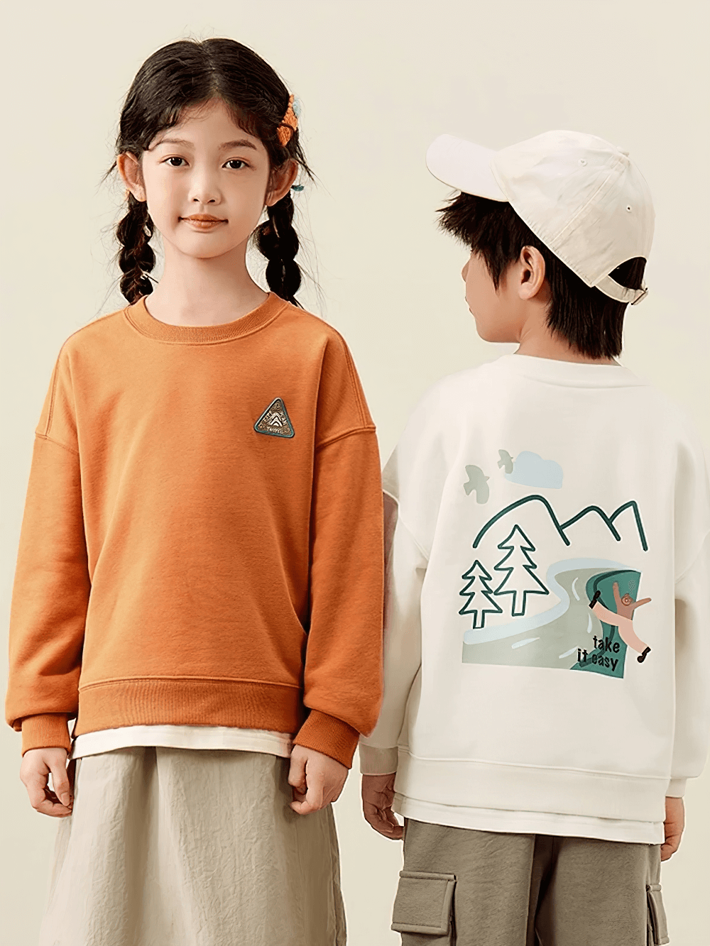 Two kids wearing trendy long-sleeved sweatshirts, one with vibrant mountain design and 'Take it Easy' print. Ideal for adventurous spirit.