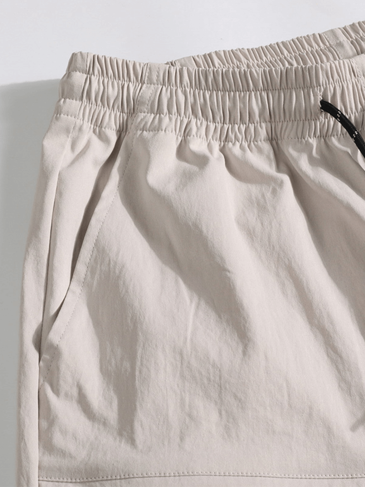 Close-up of khaki loose breathable drawstring calf-length men's shorts with pocket detail, made from lightweight spandex and polyester.