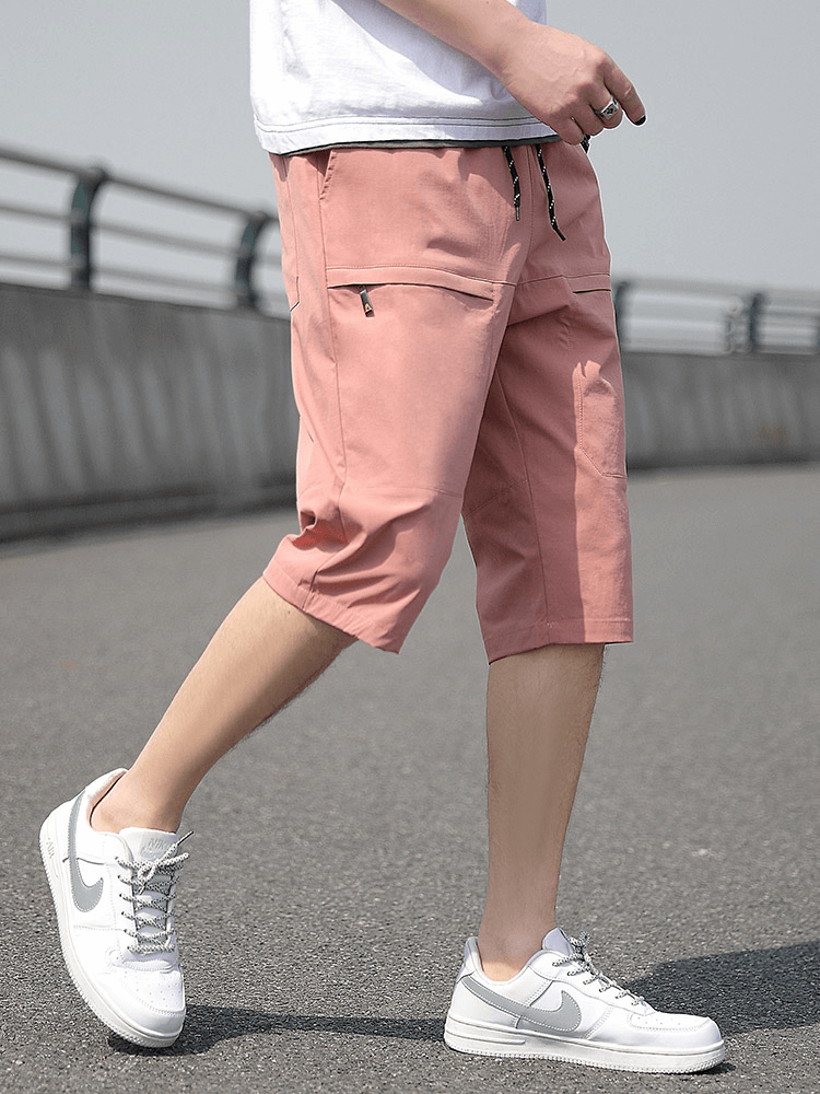 Man wearing pink loose breathable drawstring calf-length shorts with pockets, walking on pavement in white sneakers for a stylish look.