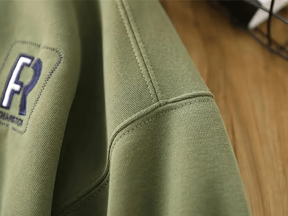 Close-up of a green cotton pullover with contrast stitching and elbow patches, perfect for casual everyday wear.