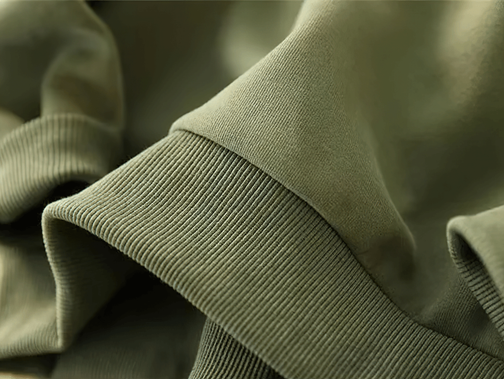 Close-up of loose cotton pullover fabric in olive green, showcasing contrast patch detailing, perfect for casual and everyday wear.