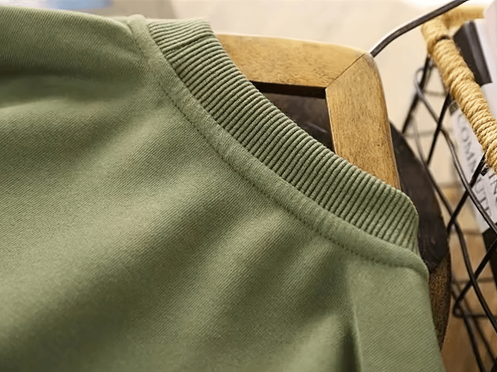 Close-up of green loose cotton pullover collar on wooden hanger, showcasing casual yet stylish everyday wear.