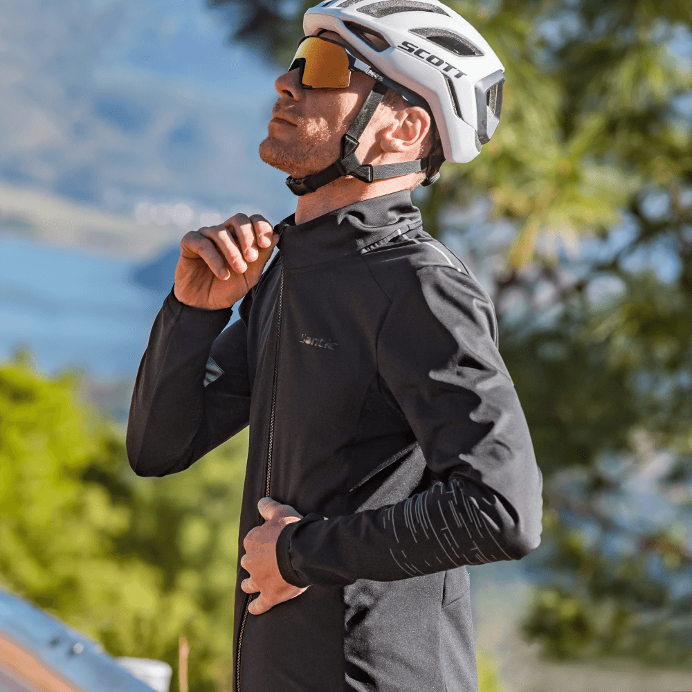 Male cyclist wearing thermal jacket, adjusting zipper, wearing helmet and sunglasses, ready for a cold weather ride in scenic landscape.