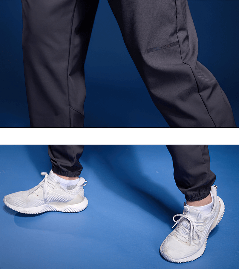 Men's black elastic waist joggers with zipper pockets, perfect for running, shown with white sneakers.