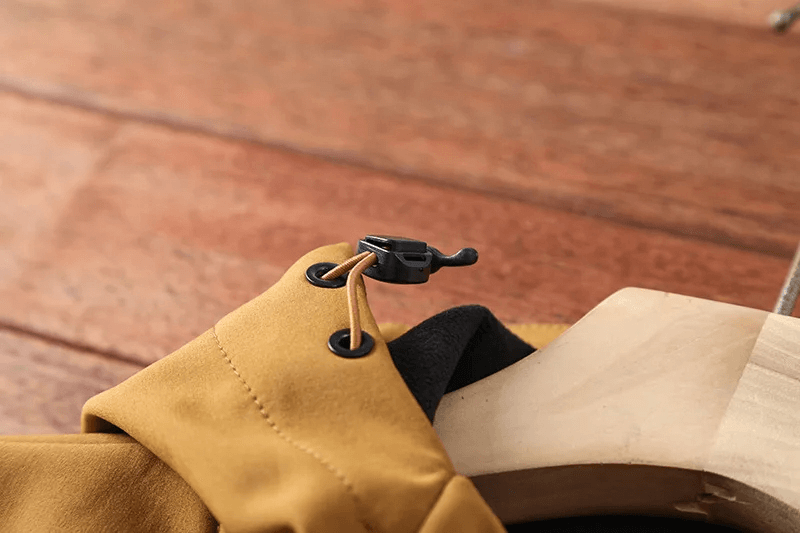 Close-up of a waterproof camping jacket hood drawstring, showcasing durable stitching and toggles on a wooden hanger.