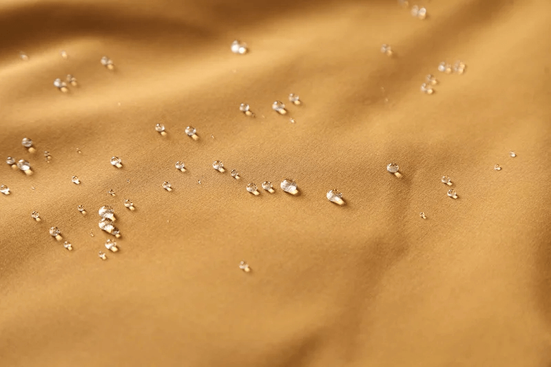 Close-up of water droplets on waterproof outdoor jacket fabric showing its water resistance.
