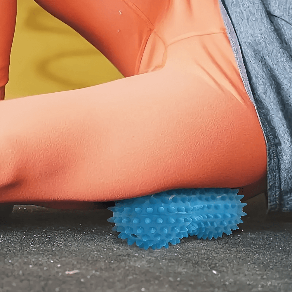 Spiky blue peanut-shaped massage ball used for muscle relief on leg muscles during fitness routine.