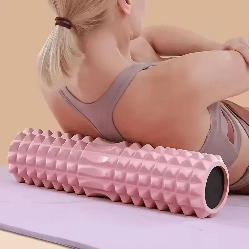Woman using pink Eva foam roller for deep tissue massage and muscle relaxation on yoga mat.