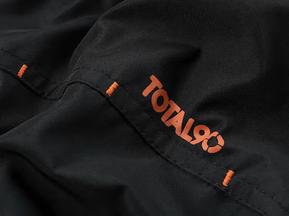 Close-up of black men’s tracksuit with Total90 logo and orange stitch accents, highlighting the athletic and breathable design.