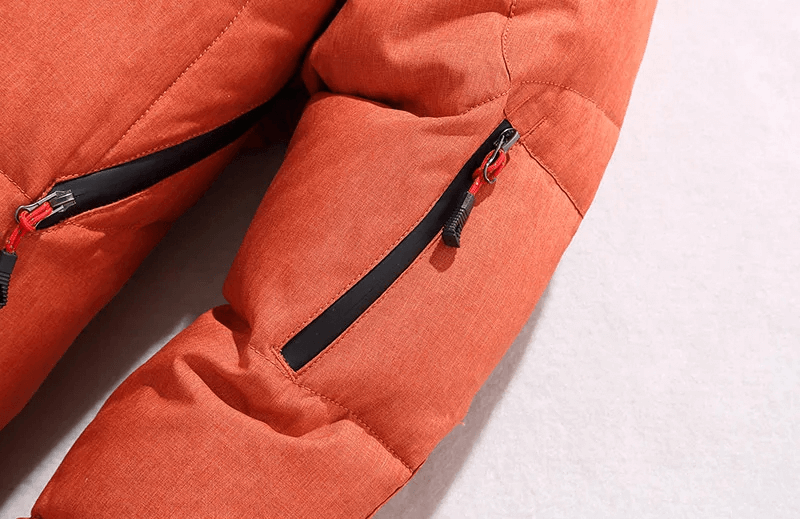 Close-up of men's orange windproof ski jacket sleeve with zippered pocket detail on fleece backdrop.