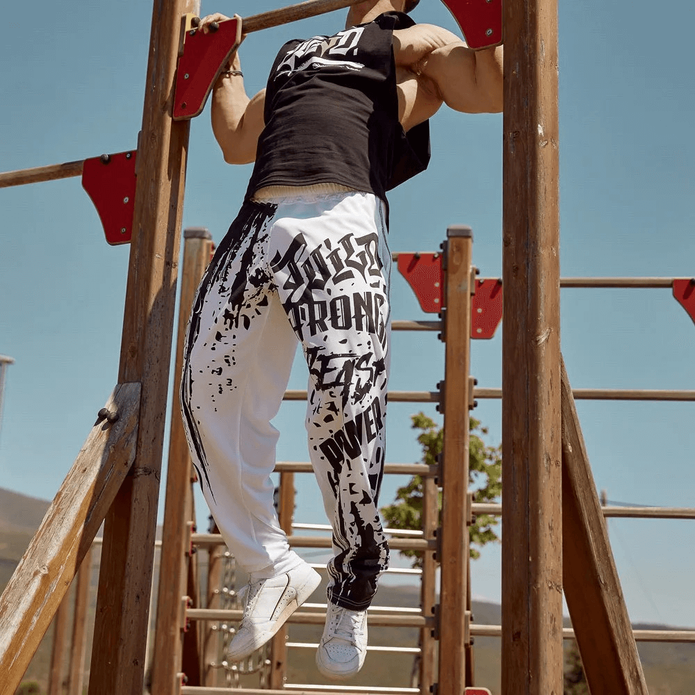 Man climbing outdoor gym bars wearing men's drip print athletic sweatpants, showcasing comfort and style during workout.