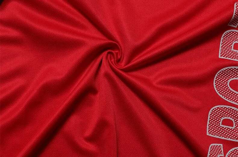 Red athletic fabric with stylish letter pattern, showcasing texture and design in a men's soccer jersey.