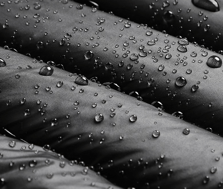 Close-up of black quilted fabric with water droplets showcasing the waterproof feature of a men's insulated down vest.