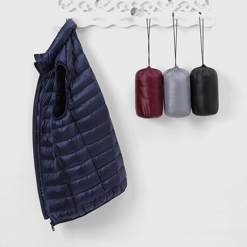 Men's quilted lightweight down vest with zipper in navy blue hanging next to three matching compact bags.