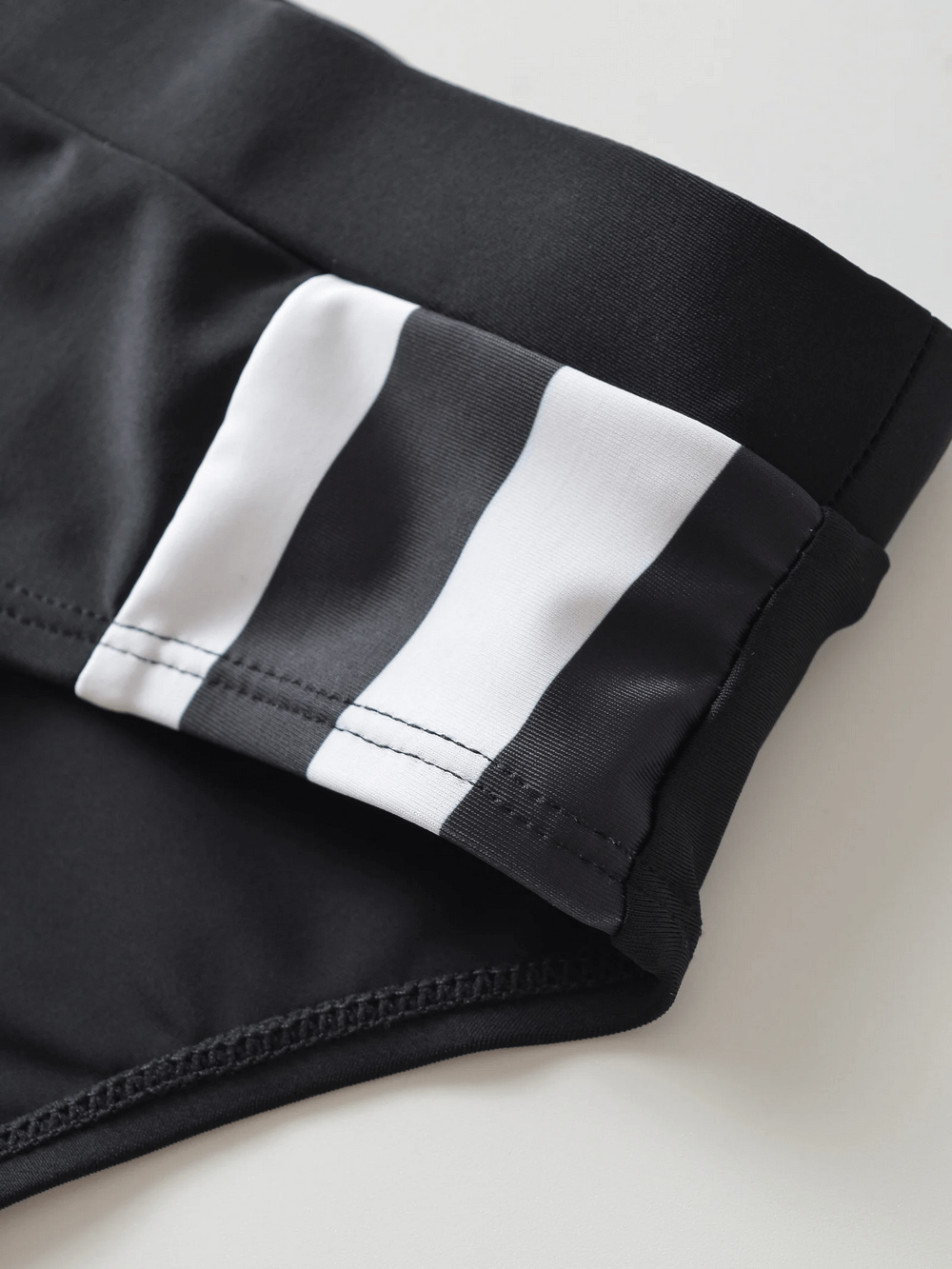 Close-up of men's swim briefs with black and white striped drawstring waistband for secure fit and style.