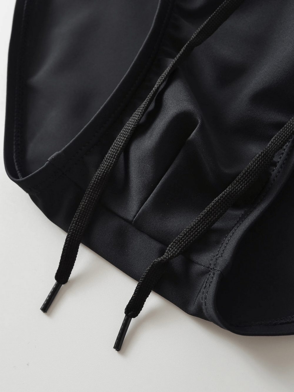 Close-up of men's black swim briefs with a drawstring waistband, featuring sleek fabric. Perfect for beachwear and swimming.