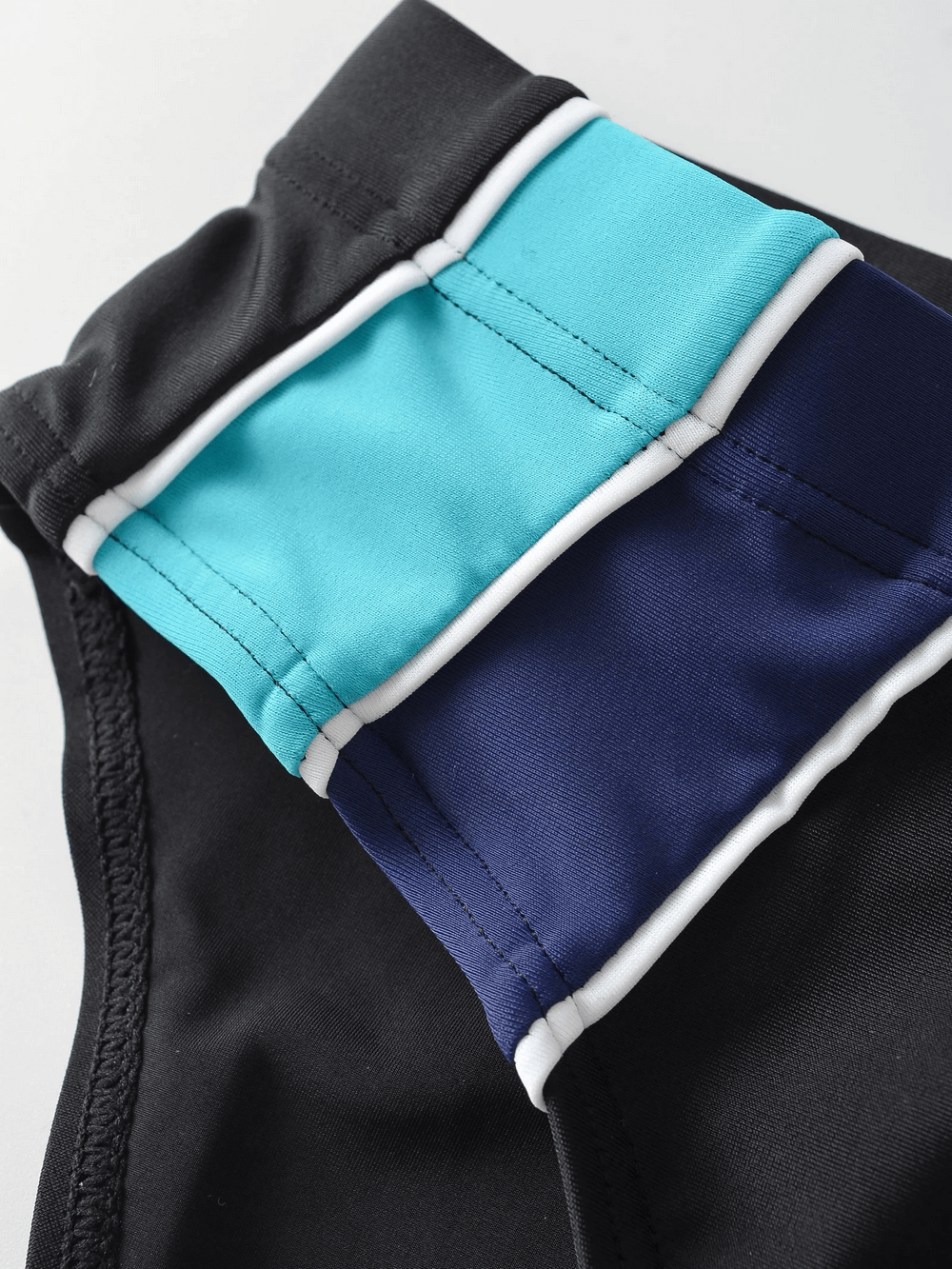Close-up of men's swim briefs in black, teal, and navy with drawstring waistband, showcasing durable beachwear design.
