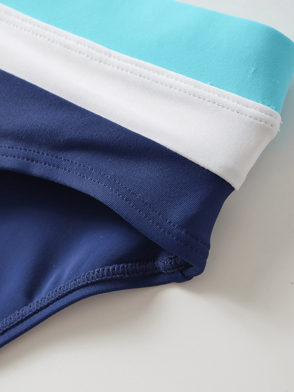 Close-up of men's mid-rise swim briefs with drawstring, featuring a stylish color-block design in blue, white, and turquoise.